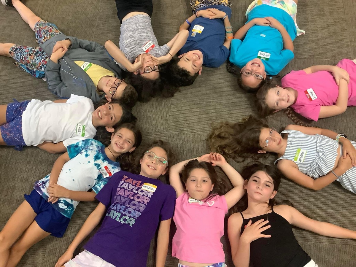 Kids lying in a circle, heads together, smiling